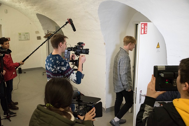 Ein Filmteam begleitet einen jungen Mann beim Betreten eines Raums durch eine Tür