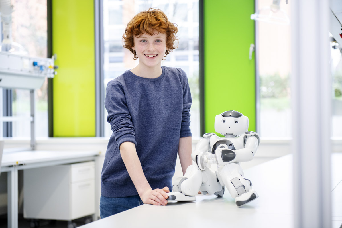 Ein rothaariger Junge steht neben einem Roboter.