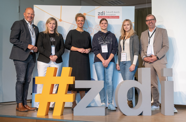Landrat Frank Rock, Bürgermeisterin Susanna Stupp, Ministerin Ina Brandes, Schülerin Lena Engel, Chemielaborantin Pia Münstermann und zdi-Koordinator Axel Tillmanns stehen nebeneinander hinter dem #zdi-Logo