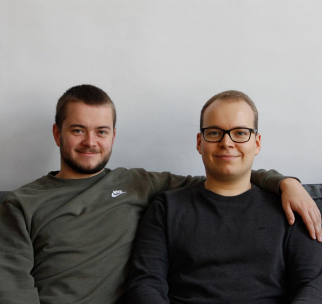 Das Foto zeigt Stefan und Philipp Lindner. Sie sitzen nebeneinander vor einer weißen Wand und lächeln in die Kamera. Stefan hat den Arm um Philipp gelegt.