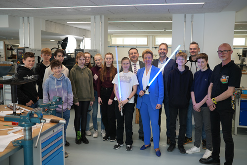 Das Foto zeigt eine Gruppe von Menschen, darunter viele Schüler:innen. Vorne in der Mitte steht Ministerin Ina Brandes. Sie hält ein blau leuchtendes Lichtschwert in der Hand.