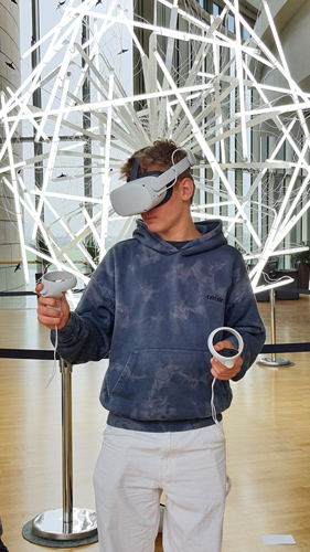Das Foto zeigt einen Jungen, der eine VR-Brille trägt. Er steht vor einer futuristisch aussehenden Lampe. Am Stand von zdi.NRW auf der Gamescom kann man auch VR-Brillen testen.