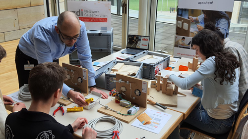 Eine Gruppe junger Menschen bearbeitet Handwerksstationen zum Thema Elektronik und Tischlern.