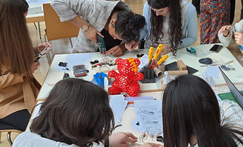 Das Foto zeigt eine Gruppe Mädchen, die um einen Tisch sitzt und ein elektrisches Draht-Spiel zusammenbaut.