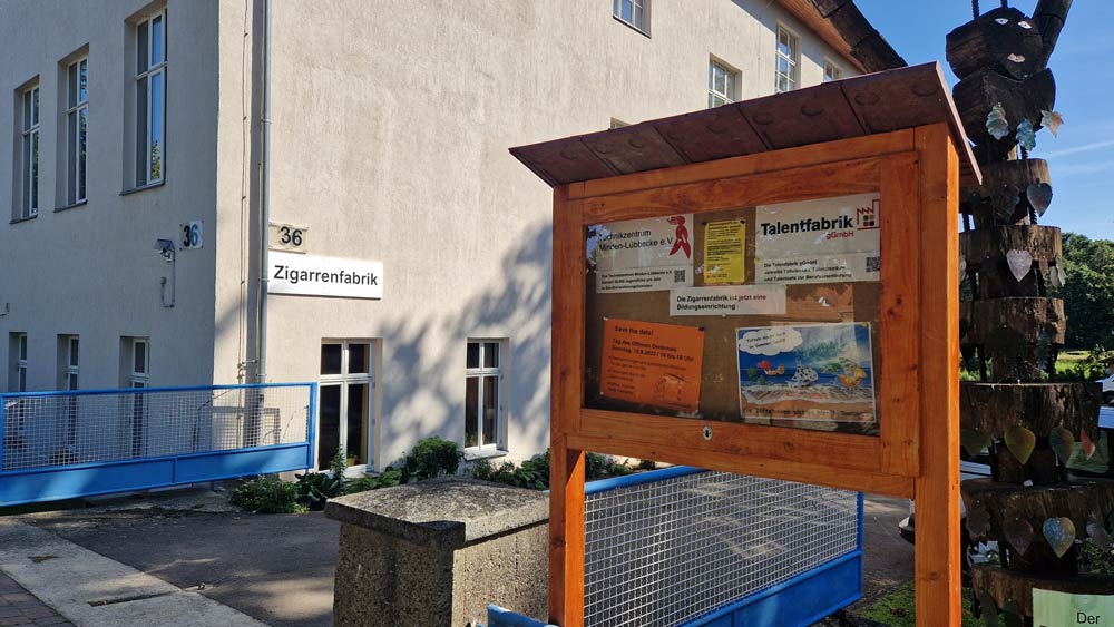 Das Foto zeigt die Einfahrt des Technikzentrums. Es hat die Hausnummer 36, darunter steht Zigarrenfabrik. In einem hölzernen Info-Kasten finden sich Informationszettel zum Technikzentrum und zur Talentfabrik.