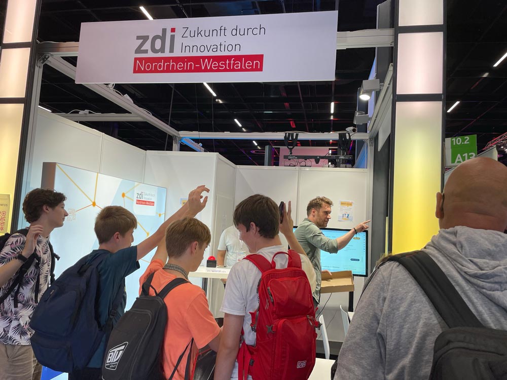 Das Foto zeigt den Stand von zdi.NRW auf der Gamescom. Vier Jungen machen beim MINT-Quiz mit.