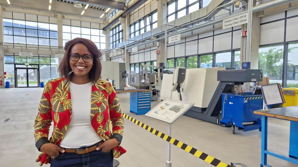 Phyllis Ndugire steht in einer Halle mit Maschinen.