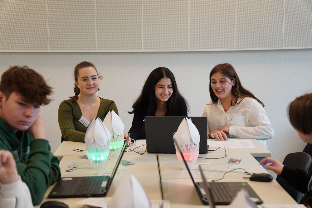 Eine Gruppe von Menschen sitzt beim zdi-Mädchen-Camp mit Laptops an einem Tisch.