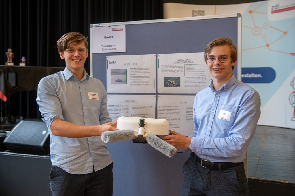 Zwei junge Männer stehen vor einem Plakat des zdi-Roboterwettbewerbs.