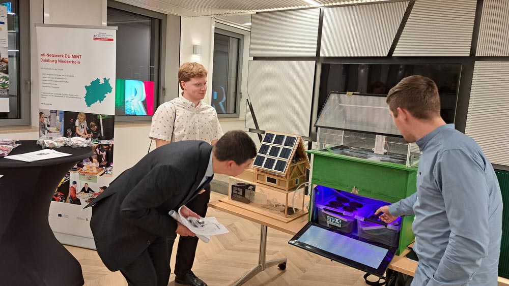 Eine Gruppe von Menschen steht um einen Tisch und schaut auf eine Indoor-Farm. Hier präsentiert das zdi-Schüler:innenlabor Hamm die Ergebnisse der zdi-Science League zur MINT-Förderung.