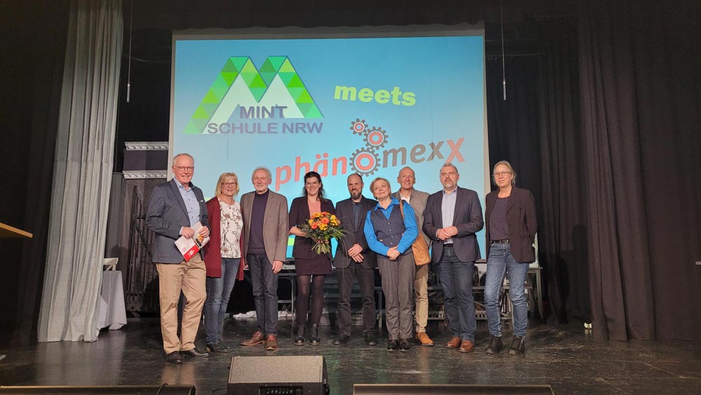 Eine Gruppe von Menschen steht auf der Bühne vor einer Leinwand.