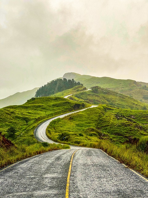 Grüne und hügelige Landschaft, die von einer Landstraße durchzogen ist.