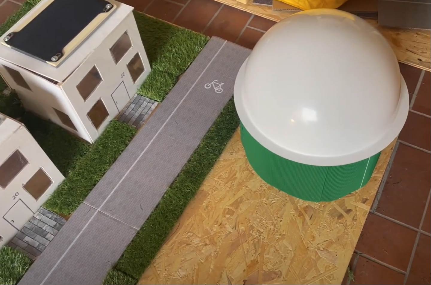 Miniaturmodellstraße mit einem Radweg neben kleinen Gebäuden und einem großen kuppelartigen Bauwerk auf der rechten Seite.