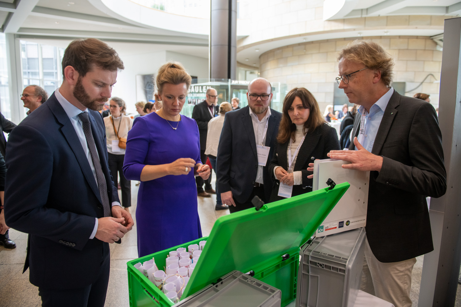 In einem modernen Gebäude begutachten im Rahmen einer Technologieschau fünf Erwachsene Geräte mit zdi-Qualitätssiegel.