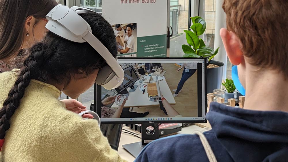 Man sieht eine Person, die mit einem VR-Headset an einer Zukunftstag-2024-Simulation teilnimmt. Andere beobachten dieselbe Simulation auf einem Laptop-Bildschirm.