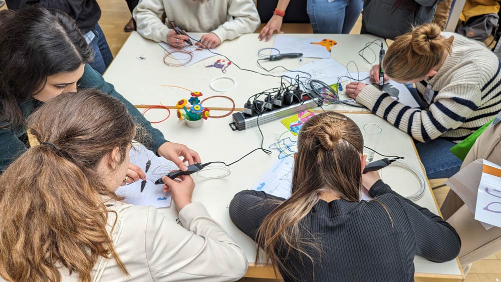 Im Zukunftstag 2024 nehmen Schülerinnen und Schüler an einem Elektronik-Workshop teil. An einem Tisch arbeiten sie mit Drähten, Schaltkreisen und Werkzeugen.