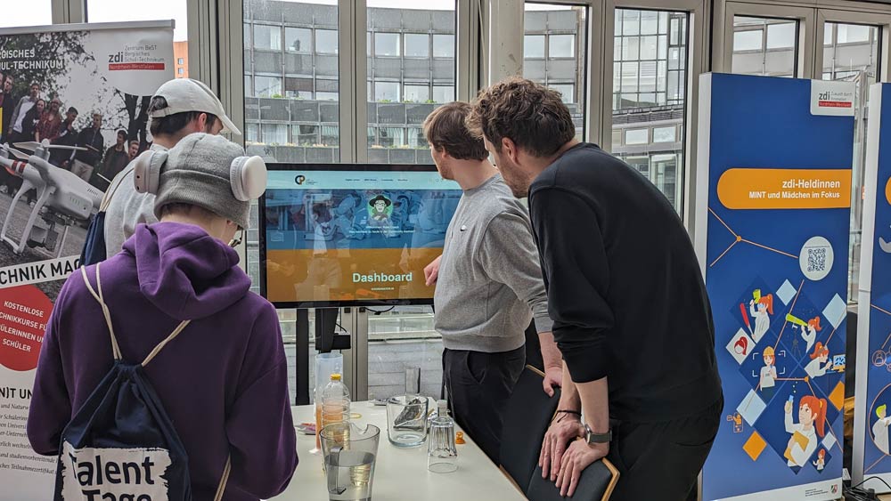 Im Zukunftstag 2024 interagieren vier Personen mit einer digitalen Dashboard-Anzeige. Der Hintergrund ist mit Informationsbannern geschmückt.