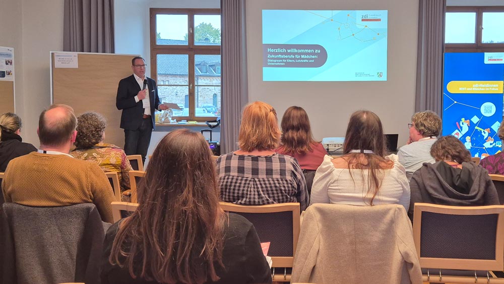 Dr. Dominik Paul begrüßt das in einem Konferenzraum sitzende Publikum der Veranstaltung „Zukunftsberufe für Mädchen“, die im Rahmen des „zdi-Heldinnen-Oktober“ stattfindet.