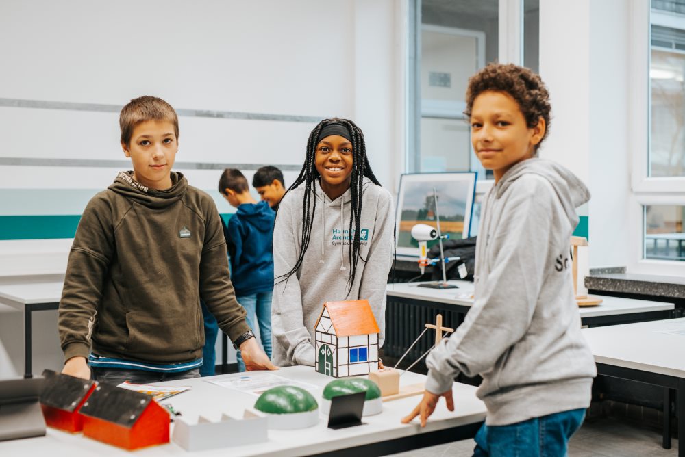 In einem PhänomexX-Labor in Krefeld stehen drei Studierende um einen Tisch und präsentieren ein Modellhaus und weitere kleine Projekte.