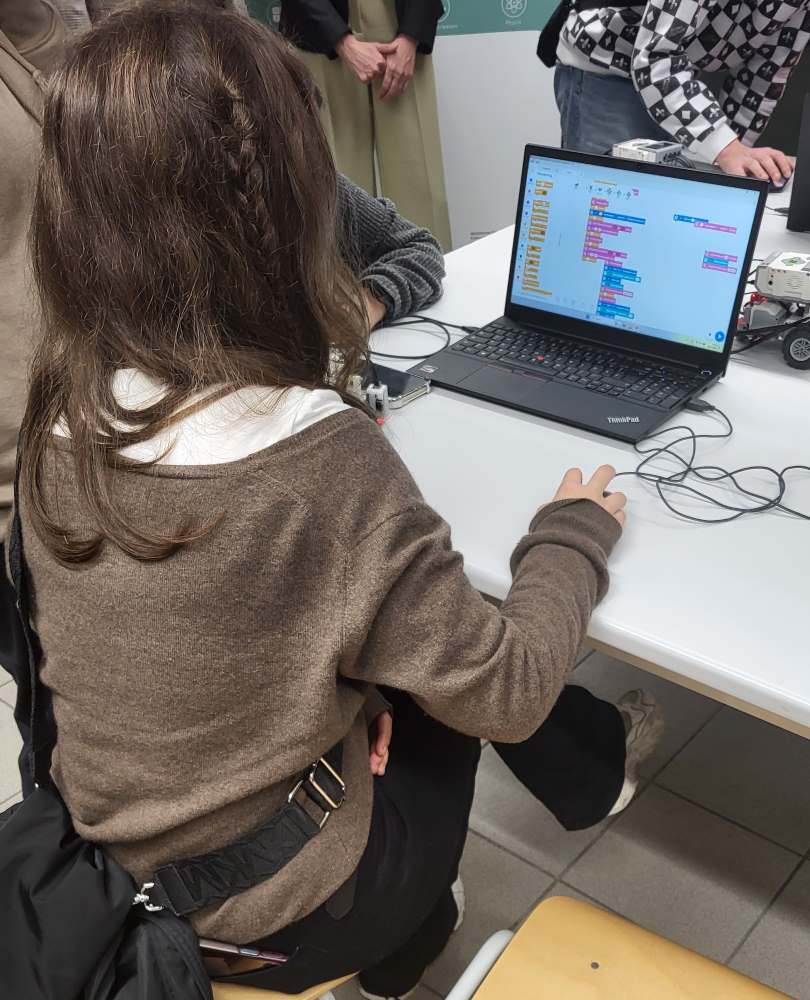 Eine Person sitzt an einem Schreibtisch und programmiert auf einem Laptop. Auf dem Bildschirm ist eine grafische Programmieroberfläche zu sehen.