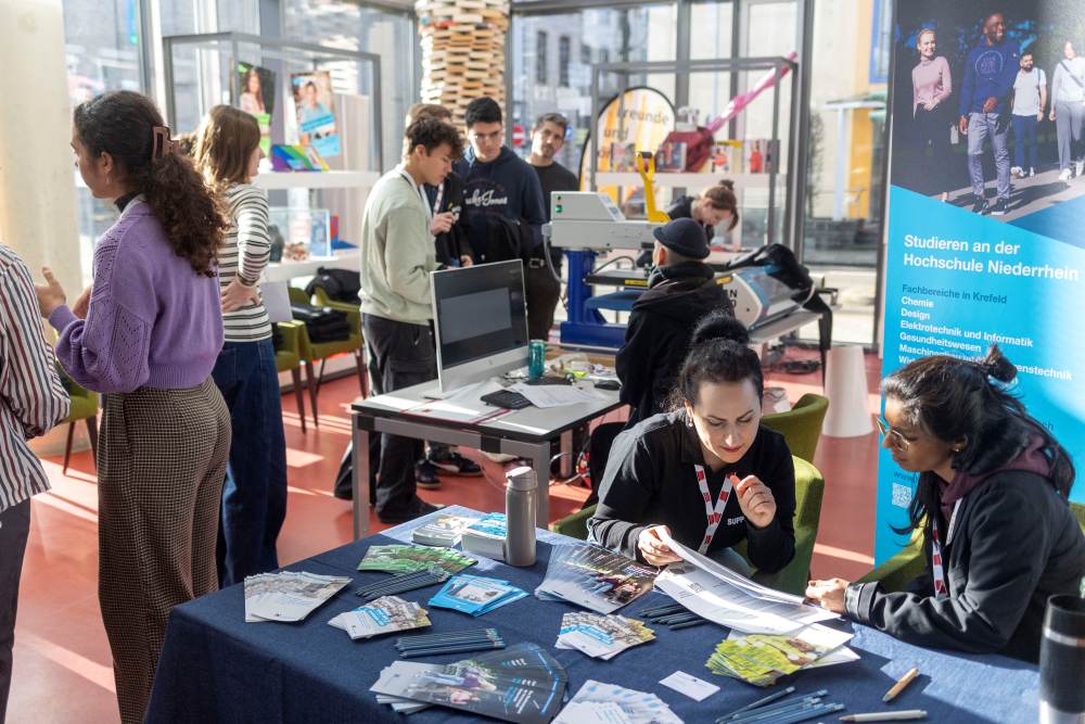 An Ständen bei der Veranstaltung KReateFUTURE 2025 interagieren die Schüler:innen eifrig mit Broschüren und betrachten diese.