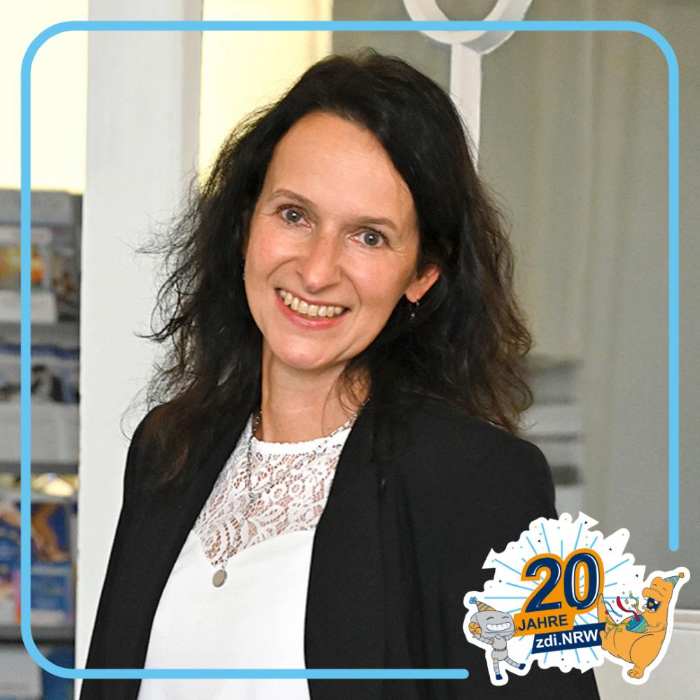 Eine Frau mit dunklen Haaren lächelt in die Kamera. Sie trägt ein weißes Top und eine schwarze Jacke. Unten rechts im Bild ist das Logo „20 Jahre zdi.NRW“ zu sehen.
