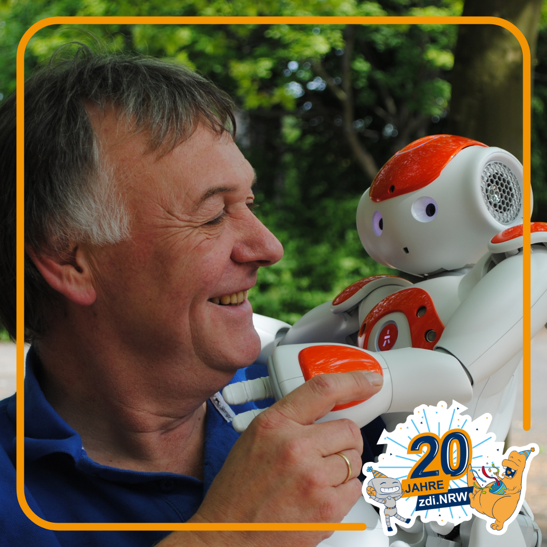 Ein Mann lächelt einen kleinen humanoiden Roboter im Freien an. Das Bild ist von einem orangefarbenen Rand eingerahmt, in der unteren Ecke befindet sich das Logo „20 Jahre zdi.NRW“, begleitet von verspielten Zeichnungen.