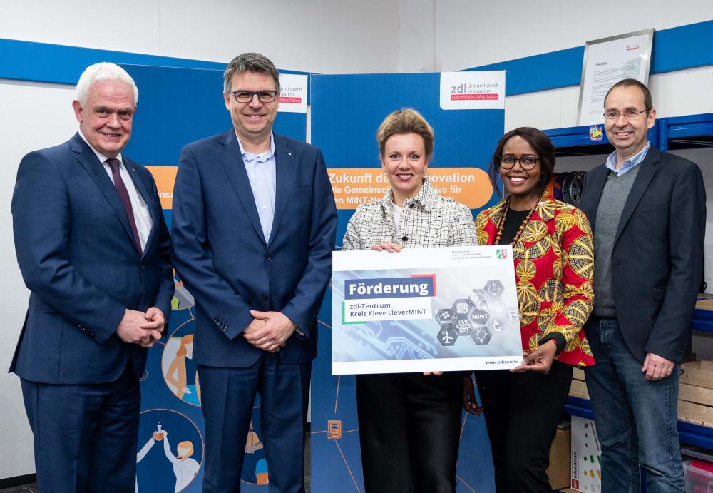 Fünf Personen stehen drinnen und halten stolz ein Schild mit der Aufschrift „Innovationsförderung“ in die Höhe. Sie lächeln vor einem Hintergrund, auf dem das Wort „Netzwerkförderung“ steht, das den Geist gemeinsamer Weiterentwicklung unterstreicht.