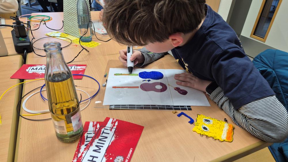 Ein Kind sitzt an einem Tisch und zeichnet mit einem 3D-Stift eine Gitarre.