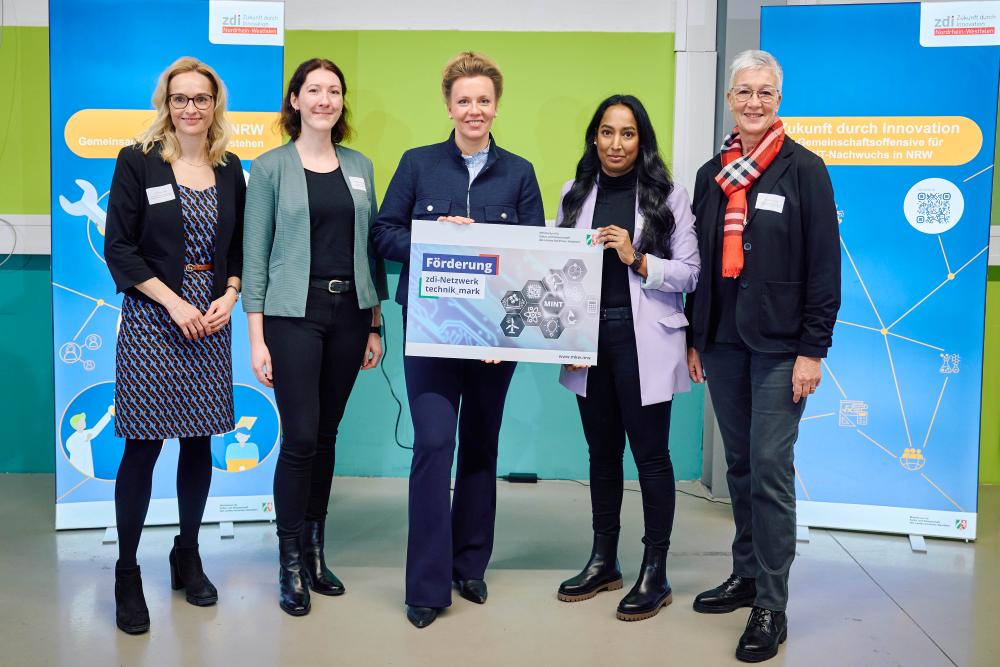 Fünf Personen stehen vor zwei blauen Aufstellern und halten ein Schild mit der Aufschrift „Förderung zdi-Netzwerk technik_mark“ in den Händen.