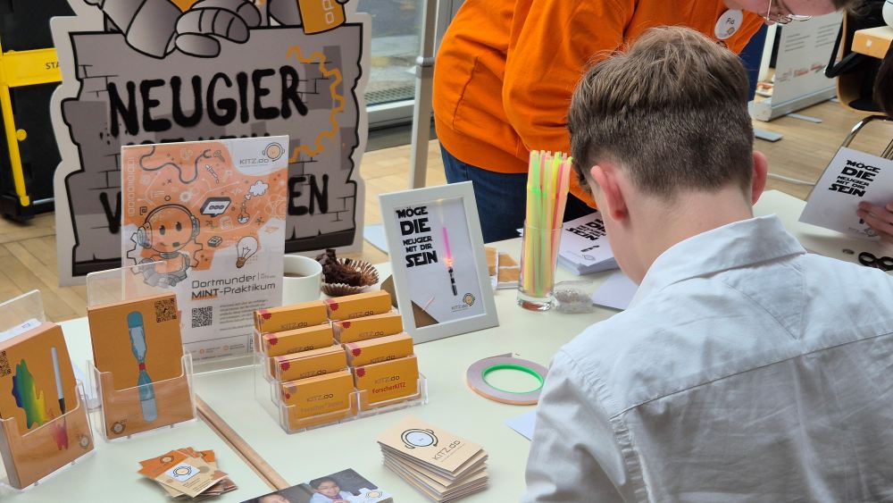 Messestand mit Informationsmaterial und einem Jungen, der sich die Exponate ansieht