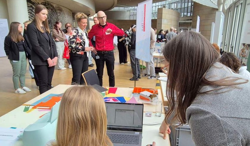 Beim Zukunftstag 2025 nehmen die Besucher an verschiedenen Aktivitäten in einem modernen Ambiente teil. Die Tische sind mit Laptops und Materialien ausgestattet und schaffen eine innovative Atmosphäre. Der helle Raum besticht durch große Fenster und eine einzigartige, geschwungene Architektur.