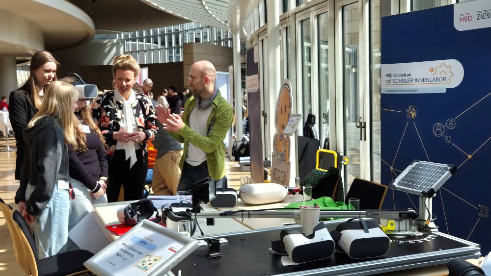 Menschen diskutieren an einem Messestand mit VR-Brillen und Solar-Modelltechnik