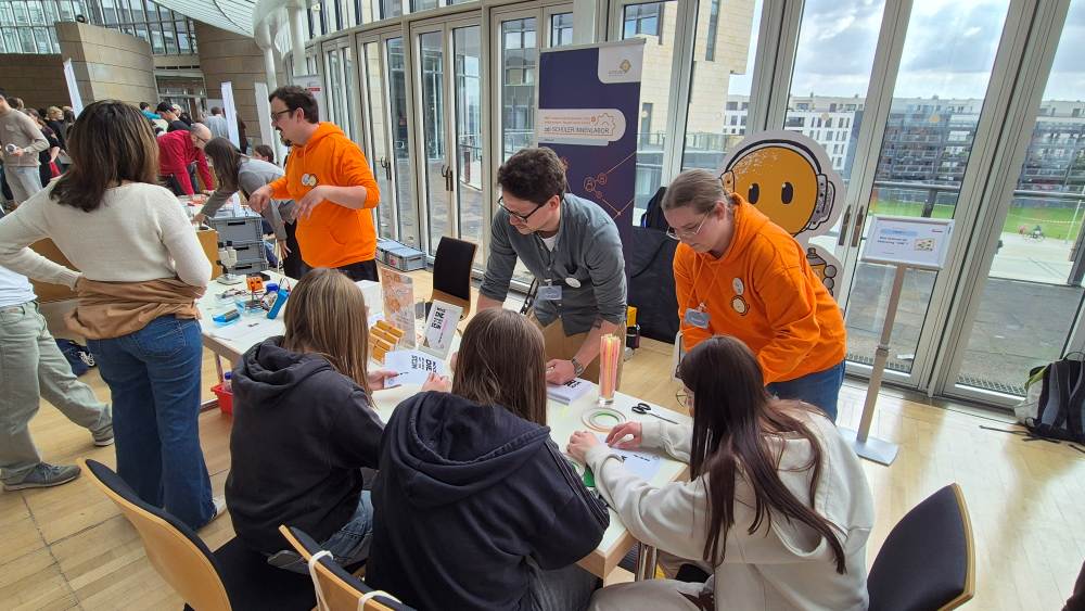 Menschen an einem Infostand bei einer Veranstaltung, die gemeinsam an einem Tisch arbeiten und sich austauschen