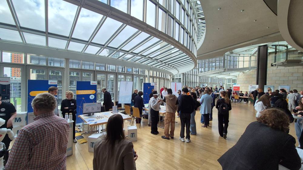 Besucher strömen durch den Zukunftstag 2025, der in einem geräumigen, modernen Saal stattfindet. Der Saal besticht durch hohe Fenster und elegante Messestände an den Wänden, die Chancen und Innovationen versprechen.