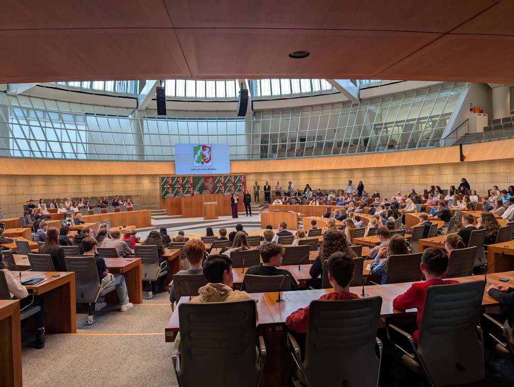 Das Foto zeigt den Plenarsaal des Landtags Düsseldorf. Schüler:innen lauschen einem Vortrag.