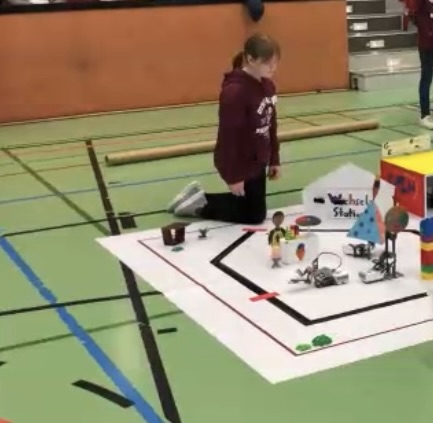 Mädchen kniet vor einem selbstgebauten Roboter-Spielplatz auf einer großen weißen Fläche in der Turnhalle