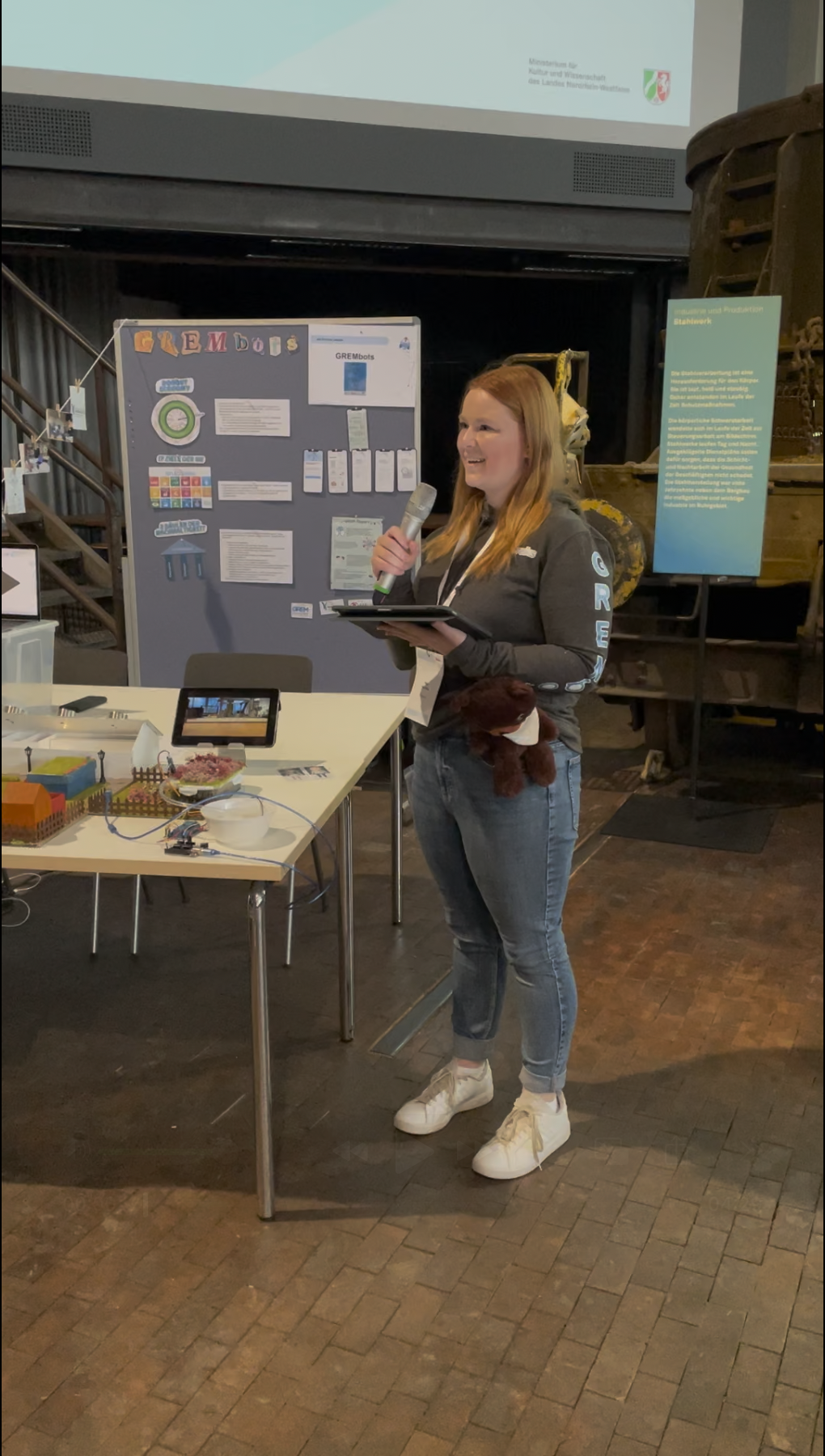 Eine Frau präsentiert ein Projekt mit Modell und Poster auf einer Veranstaltung