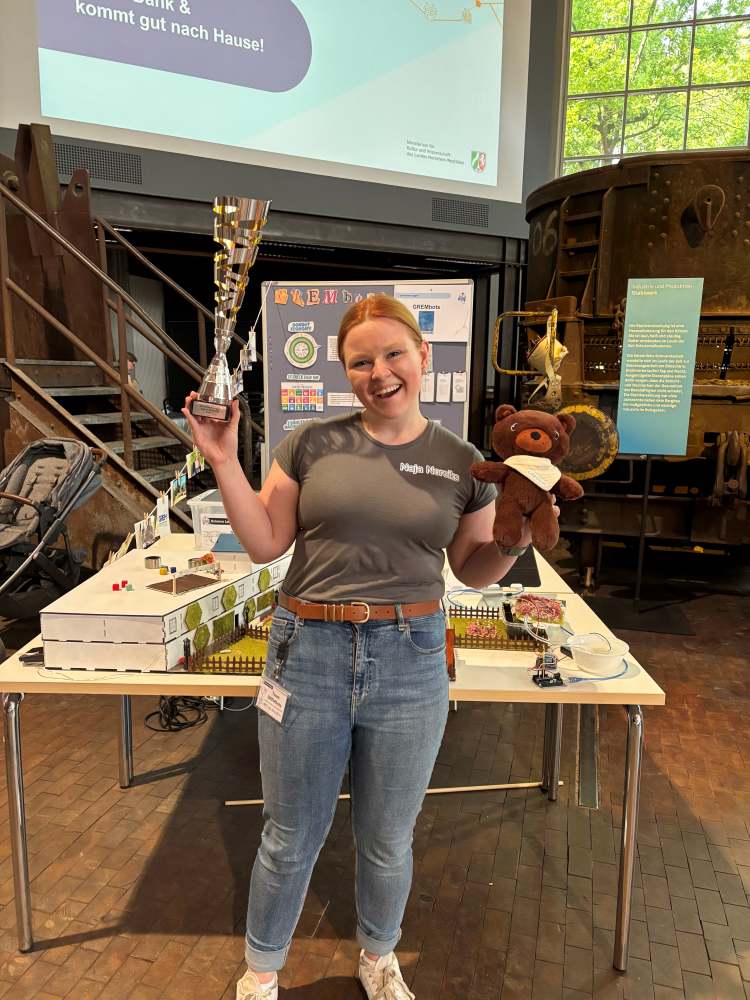 Frau hält einen Pokal und ein Stofftier vor einem Ausstellungsstand