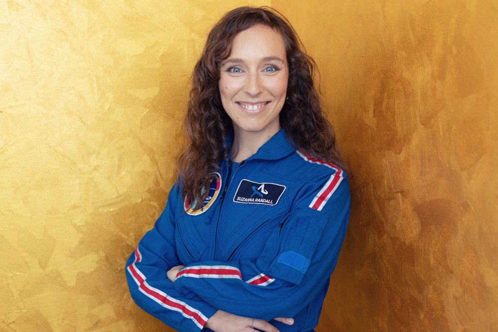Das Bild zeigt Dr. Suzanna Randall in einem blauen Overall mit Raumfahrt-Logo und einem Namensschild.