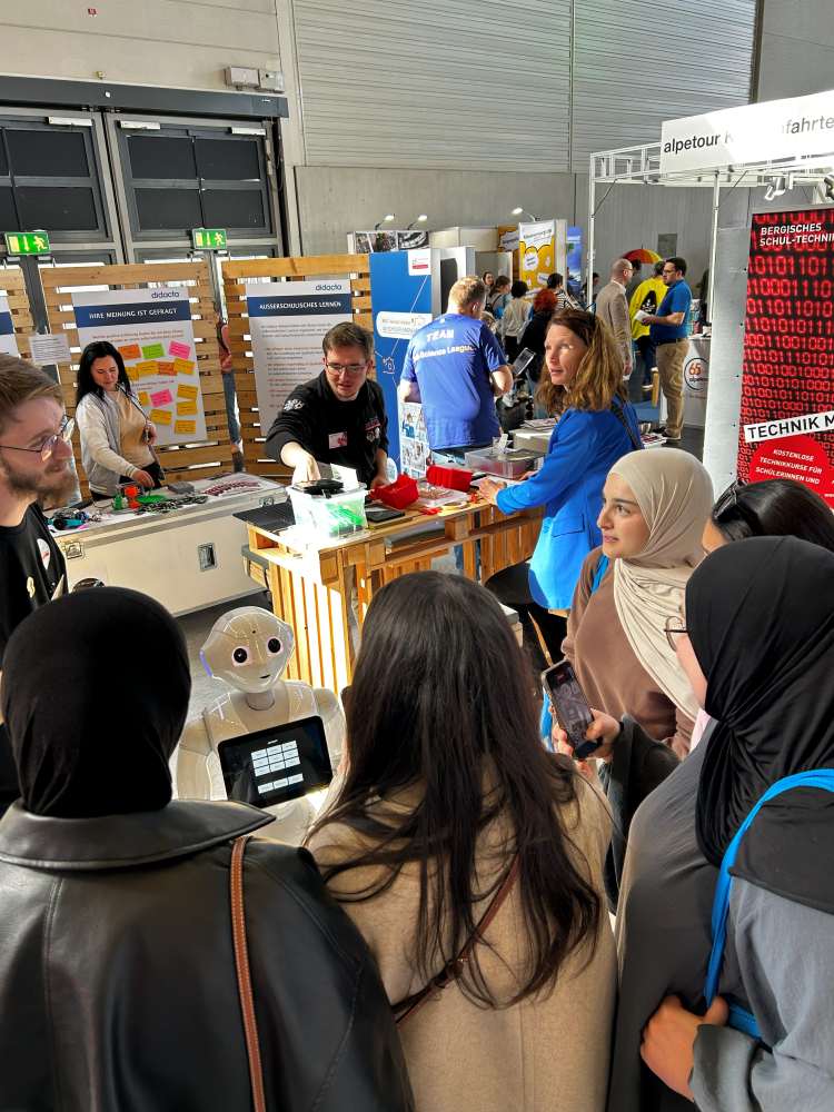 Menschen versammeln sich um einen Roboter an einem Technologie-Ausstellungsstand. Das Personal unterhält sich mit den Besuchern, und im Hintergrund sind Displays zu sehen.