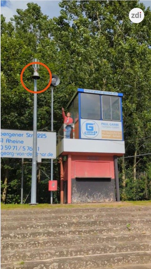 Person in einer kleinen Seilbahnstation neben einem markierten Mast mit Glocke