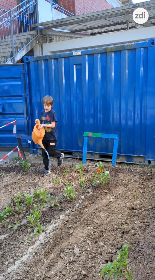 Ein Kind bewässert einen Acker vor einem blauen Frachtcontainer.