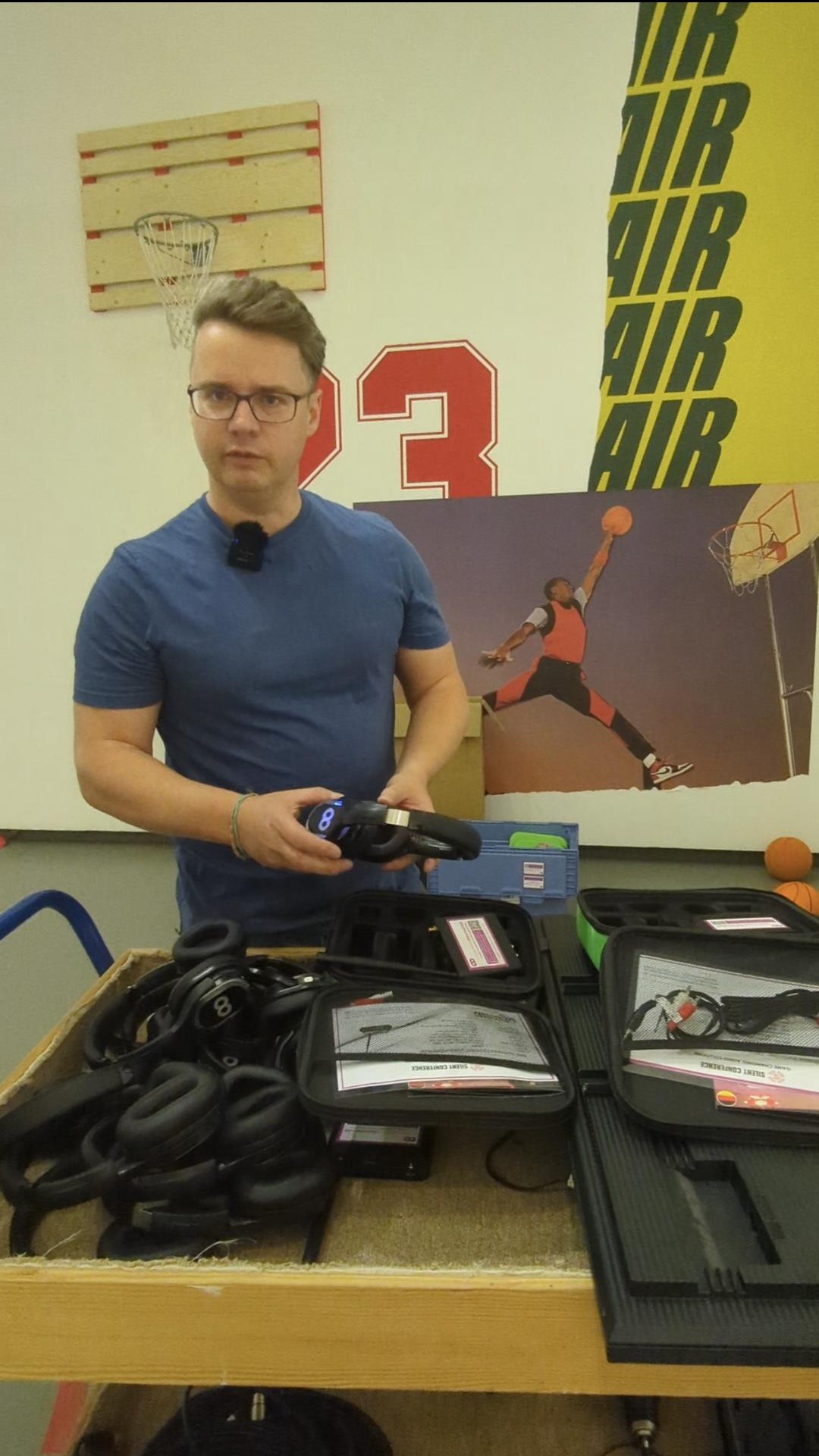Mann präsentiert Kopfhörer und Zubehör an einem Tisch in einer Sportausstellung