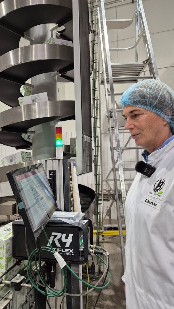 Eine Person im Laborkittel und mit Haarnetz benutzt einen Touchscreen-Computer zur Überwachung einer Produktionslinie in einer Industrieanlage.