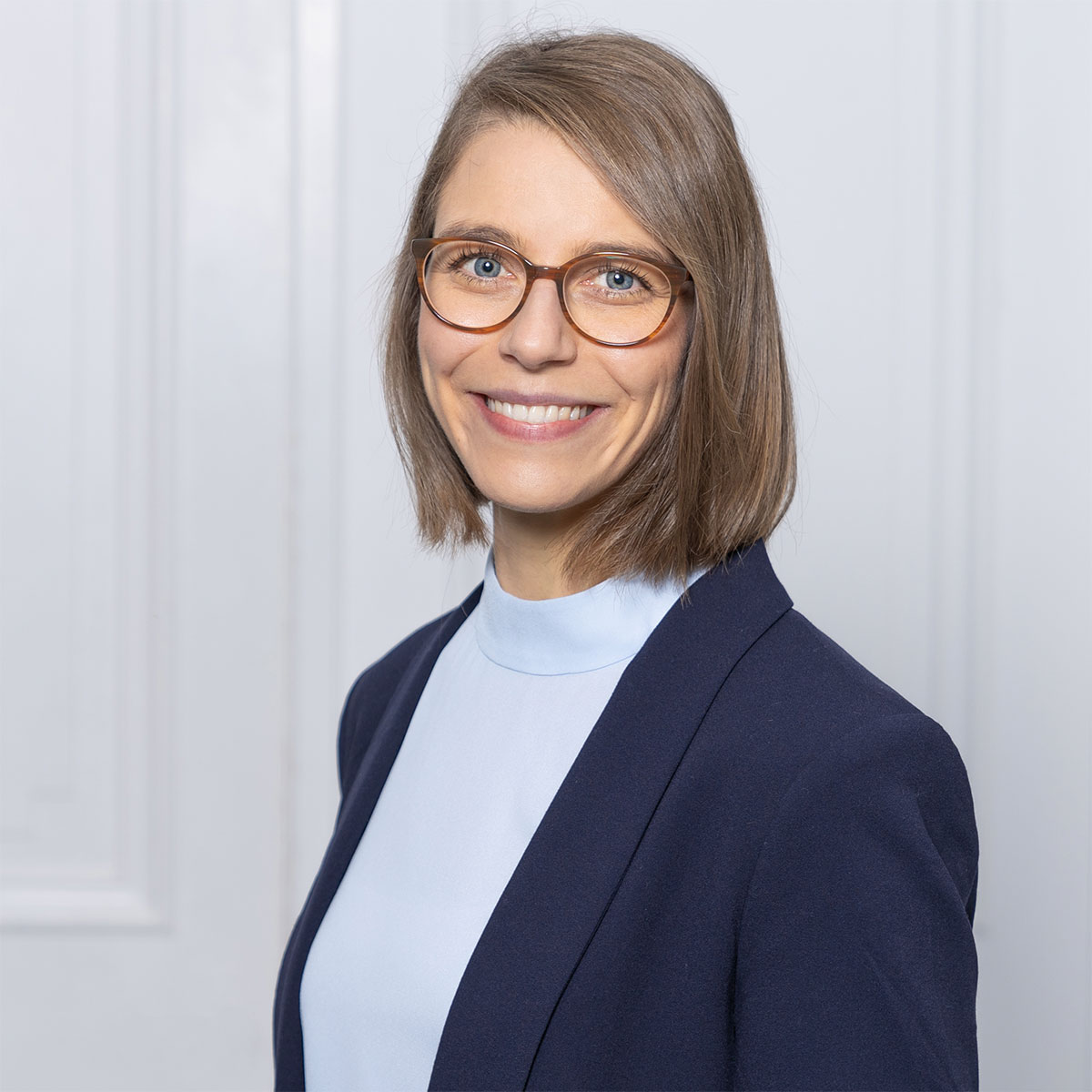 Porträt einer lächelnden Frau mit Brille in Blazer und hellem Oberteil