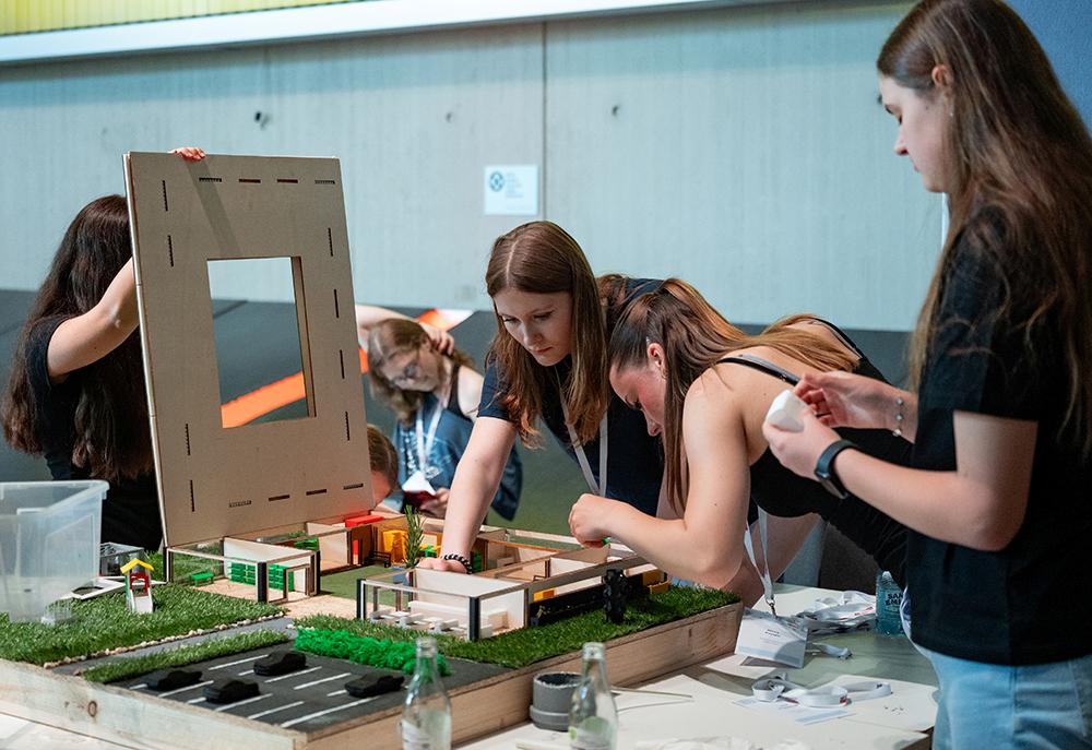 Studierende arbeiten an einem Architekturmodell mit Gebäuden, Straßen und Grünflächen
