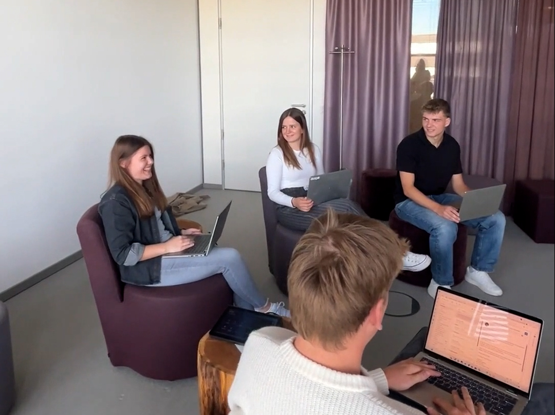 Das Foto zeigt vier Personen in einem Meeting-Raum mit Laptops auf dem Schoß. Eine davon ist Vanessa Kriebel, sie lacht fröhlich.